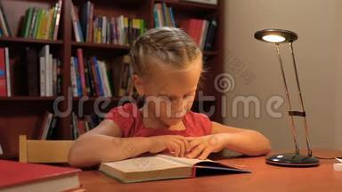 一个六岁的女孩坐在桌旁的台灯旁看书